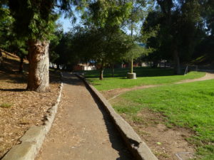 The walled concrete channel appears to be a path or bike lane. Actually it is a drain for Campus Road which does not provide a way through the park or connect with the parks paths and roads.Visible in the background is the rear wall of the bath house a prime graffiti canvas. This building, though part of the original plan, now isolates the upper park from the lower area.-Photo by Eric Warren, 10-13-2010.