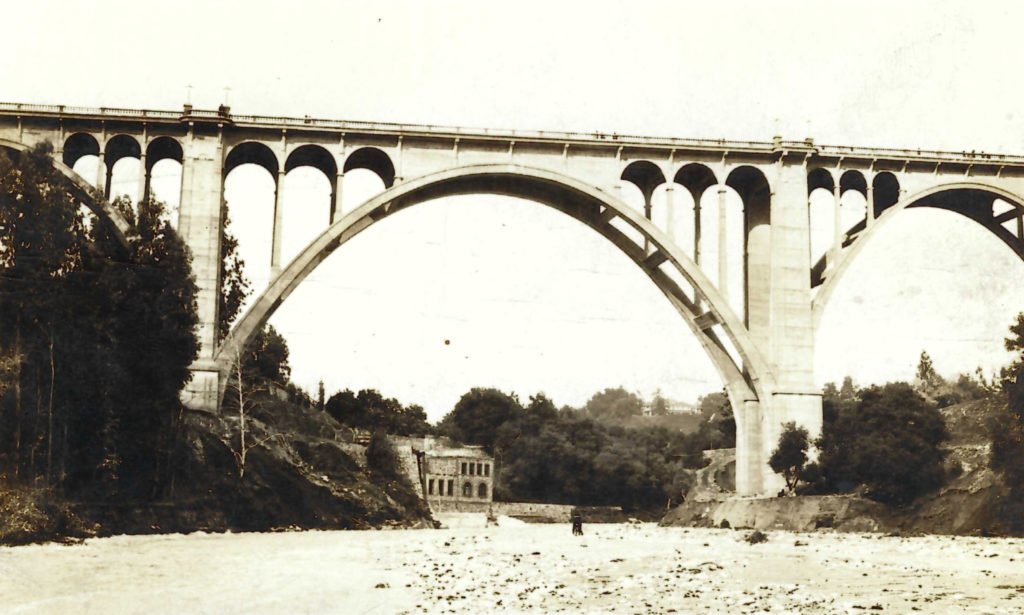 The finished bridge with the streambed in the foreground. The remains of the Scoville Bridge and its dam are visible behind the bridge columns. (ERVHS)
